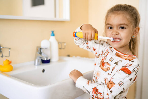 girl brushing her teeth with an electric brush, standing in the bathroom near the sink